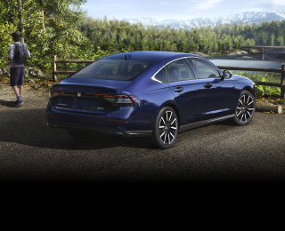 3/4 rear view of a parked blue Accord overseeing a forest and mountains. A hiker walking away from it.