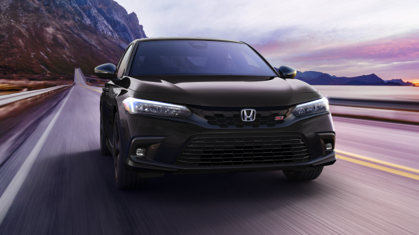 Front view of black Civic Si driving toward camera on a mountainous oceanside highway. 