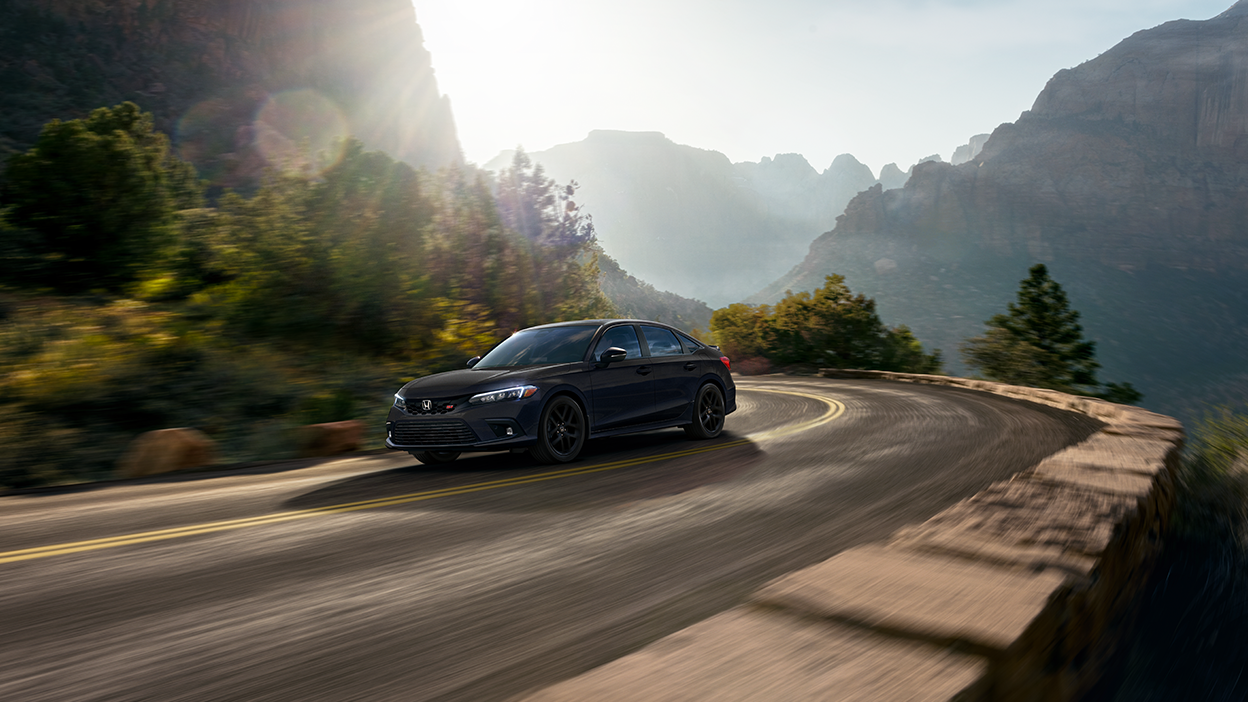 3/4 front view of orange Civic Si driving on city highway at night. 3/4 front side view of black Civic Si taking a turn on a mountain highway.