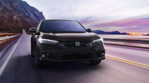 Front view of black Civic Si driving toward camera on a mountainous oceanside highway. 