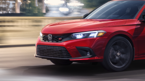 3/4 front side view of red Civic Si driving over a city bridge.