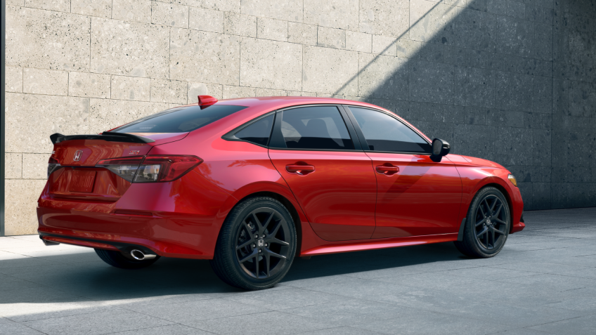 Rear sideview of a red Civic Si parked in front of a stone-walled building.