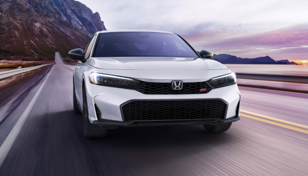 Front view of white Civic Si driving toward camera on a mountainous oceanside highway.