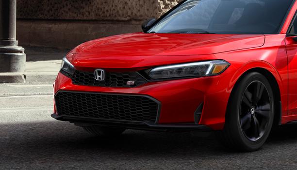 Closeup of headlight on red Civic Si driving on city street.