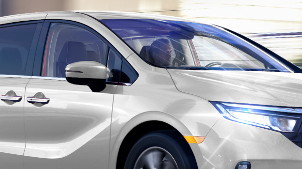3/4 side front view of white Odyssey driving in city.