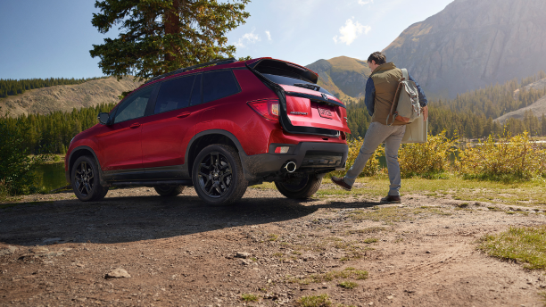 3/4 rear view of red Passport, outdoors. Man waving foot under bumper, opening trunk.