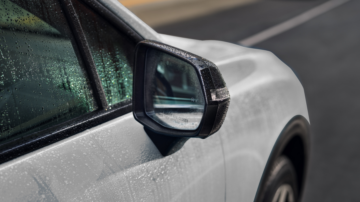 Closeup of side mirror on white Prologue covered in rain drops.