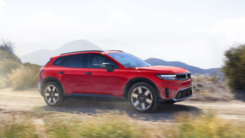 Side view of red Prologue driving on dirt desert road.