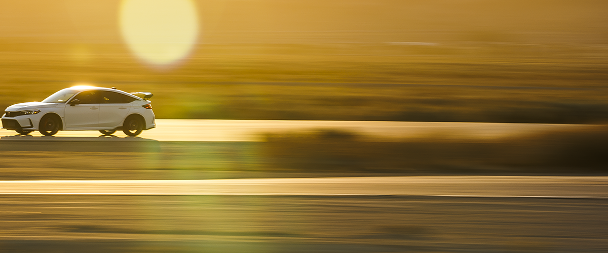 Wide shot and sideview of a white Type R driving down a highway during a desert sunset. Front is more visible. 